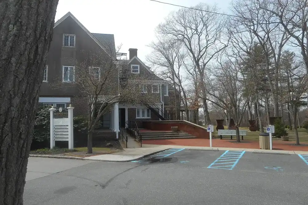 Brookwood Hall, a dark shingled historic building with a small sign and lot in East Islip, New York