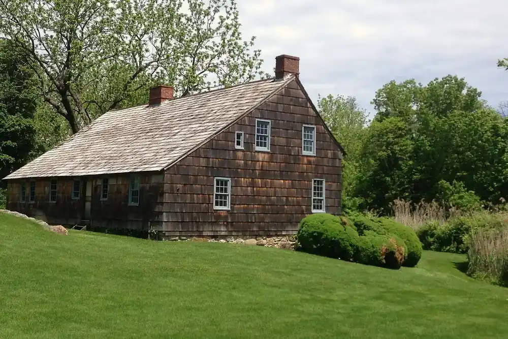 Historic Brewster House with a weathered cedar-shingle roof on a green lawn in East Setauket, New York