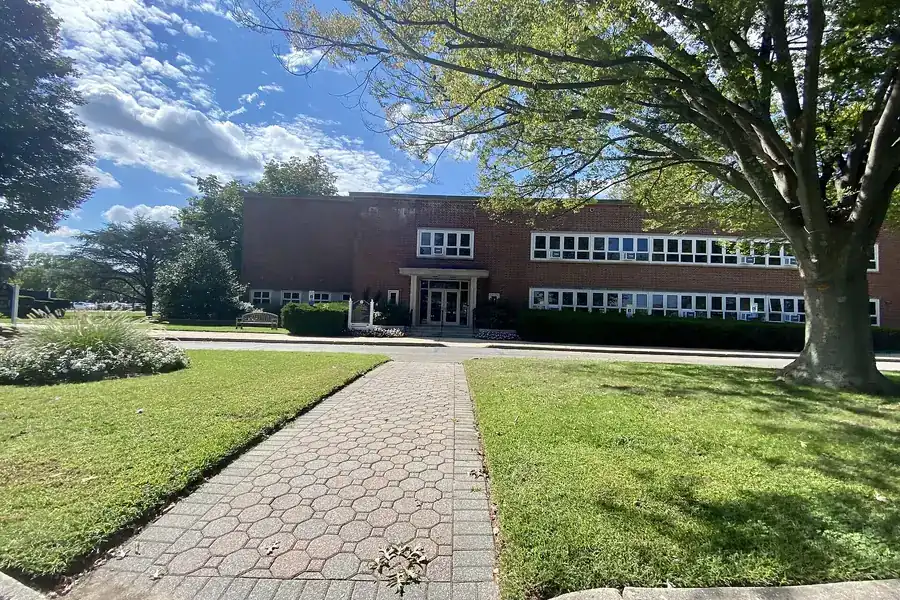 Brick paved path across the lawn to Garden City Village Hall under a blue sky