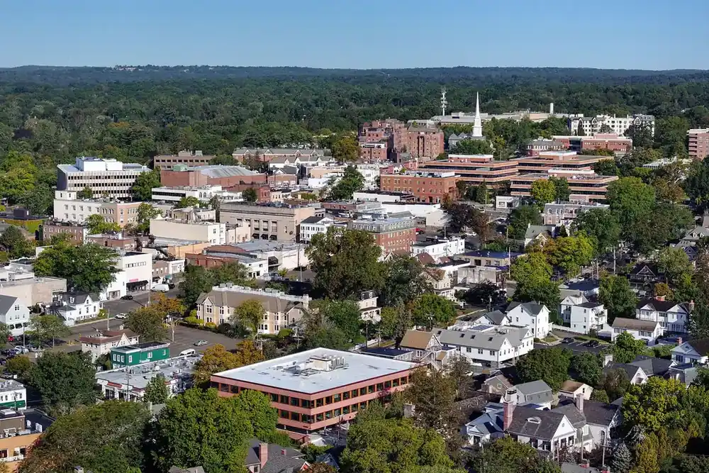 Aerial view of downtown Greenwich, Connecticut, with a white church steeple and wooded hills beyond