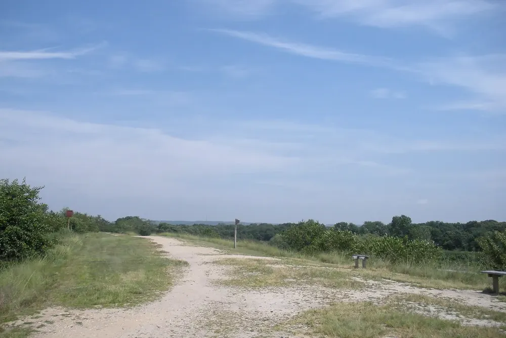 Gravel path along a grassy hilltop with trees and blue sky at the Holtsville Ecology Center