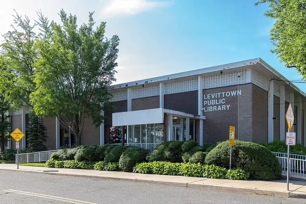 Levittown Public Library, a low brick building with trimmed hedges and a sunny sky in Levittown, New York
