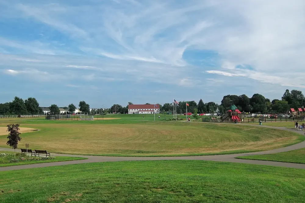 Wide green lawn with walking paths and play equipment at a park in Mount Sinai, New York
