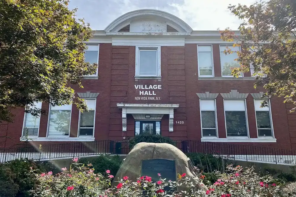 New Hyde Park Village Hall, a red brick building with a white cupola, and rose beds in front
