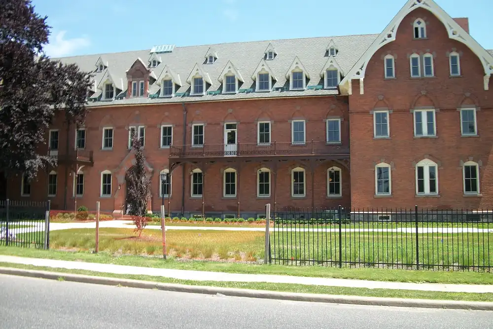 Large red brick motherhouse building with gabled dormers behind a fence in North Amityville, New York