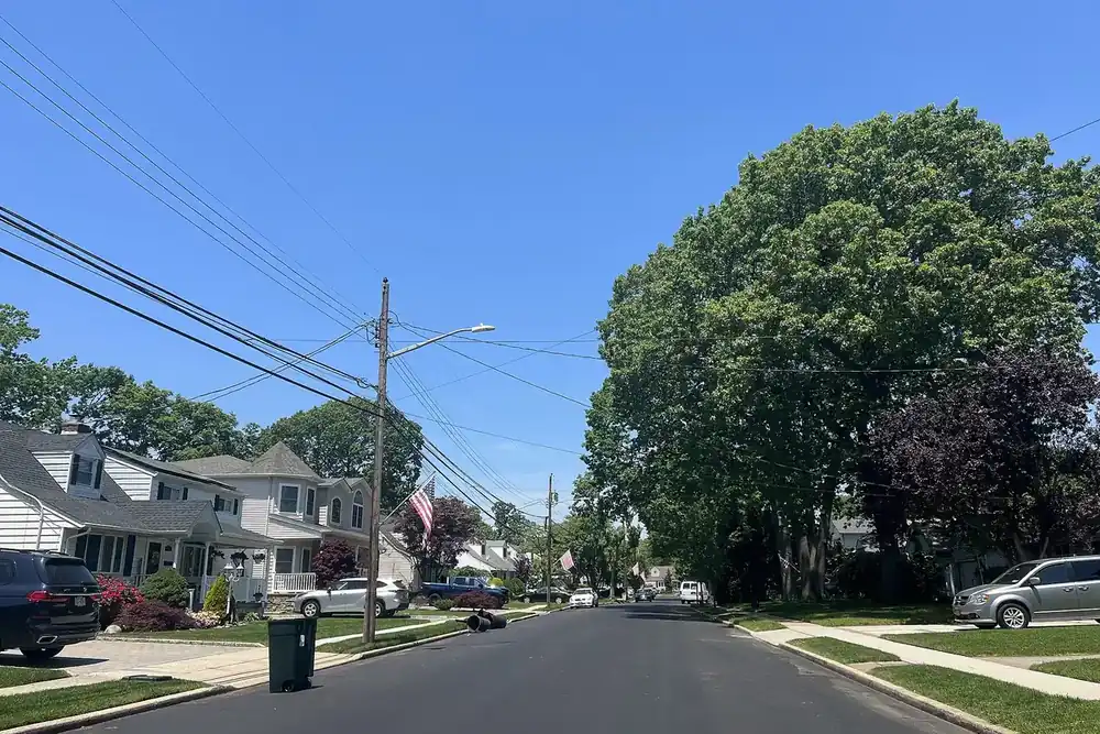Quiet tree-lined residential street with houses and parked cars in North Merrick, New York