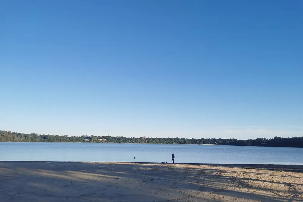 Sandy beach and calm blue water of Lake Ronkonkoma under a clear sky in Ronkonkoma, New York