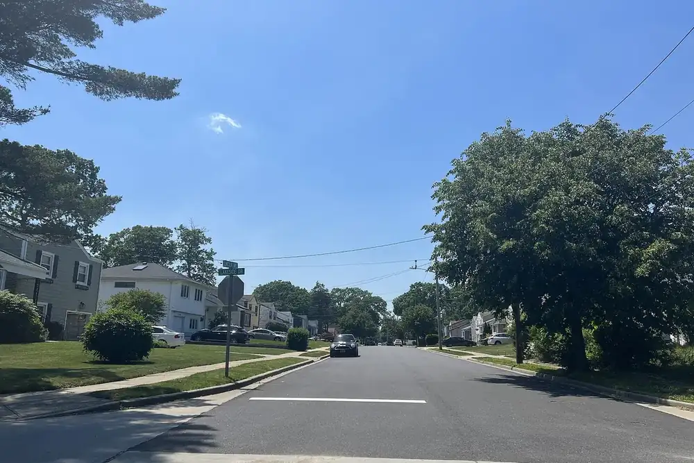 Quiet residential street with a green tree and bright blue sky in Roosevelt, New York